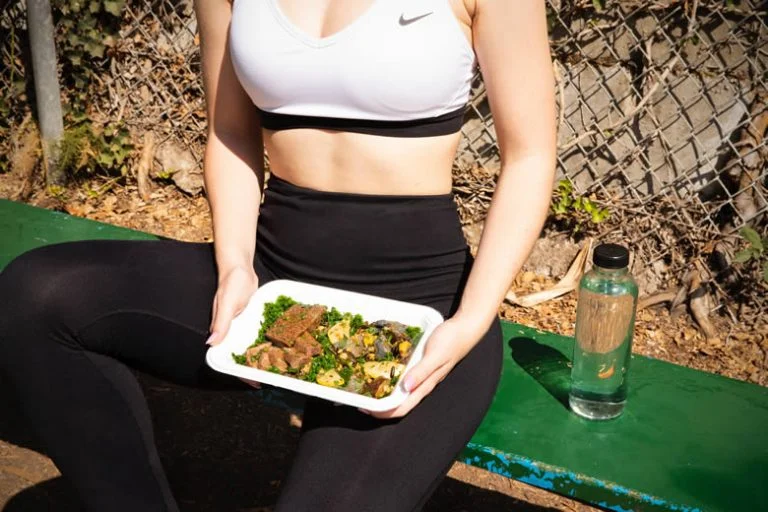 Woman sitting on a bench holding her pre-prepared lunch in her hands.
