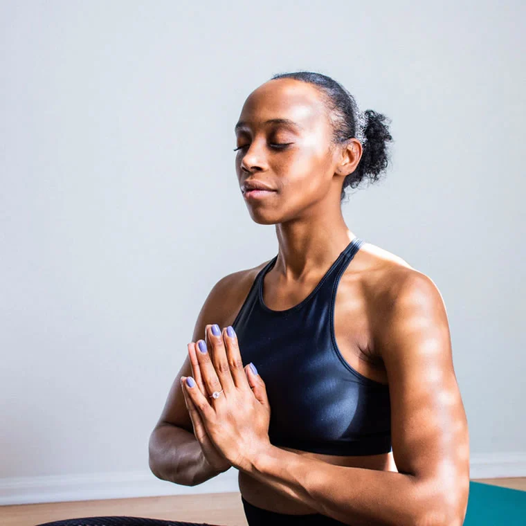 a woman sitting on a yoga mat with her hands together